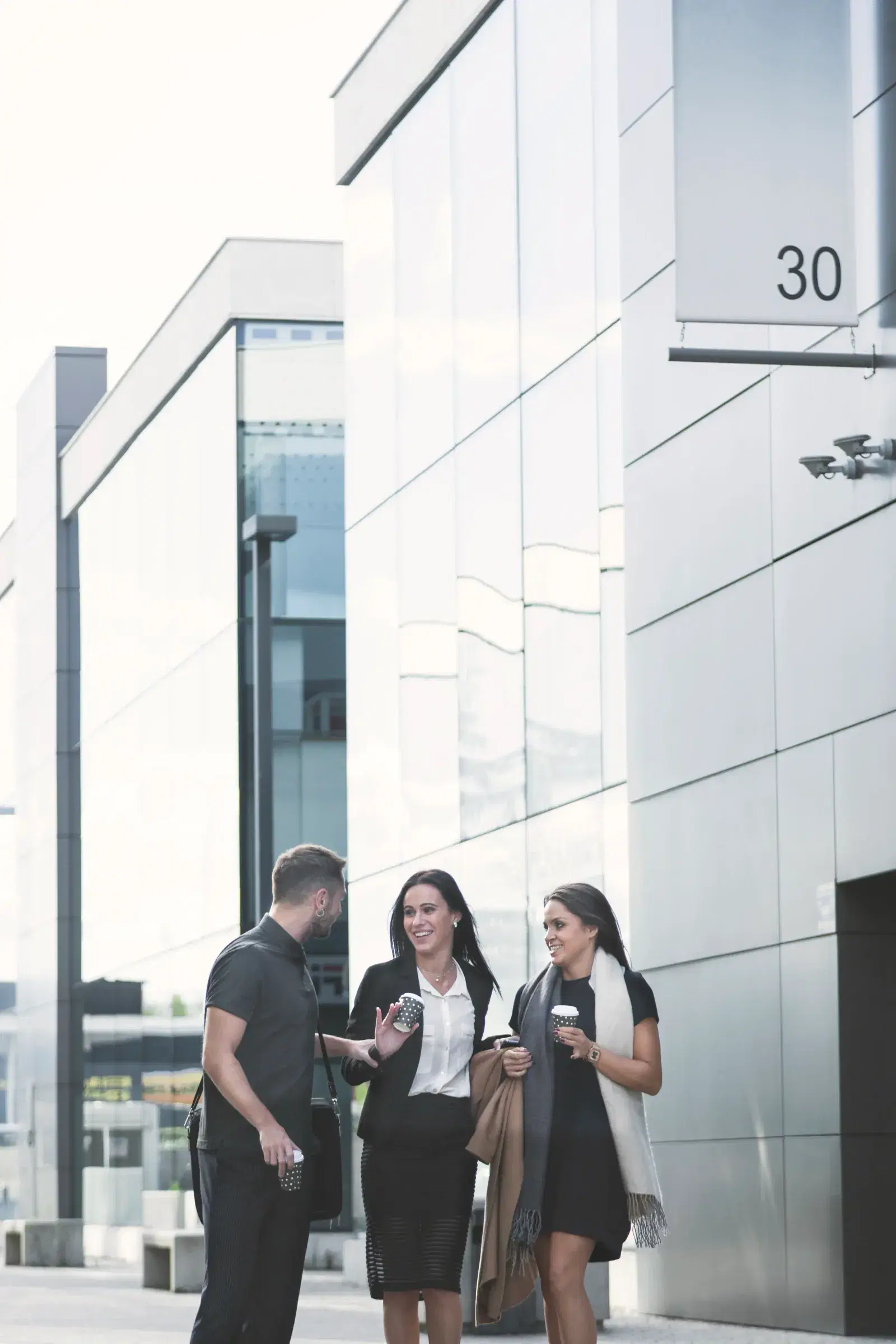 Three colleagues with coffee outside an office building