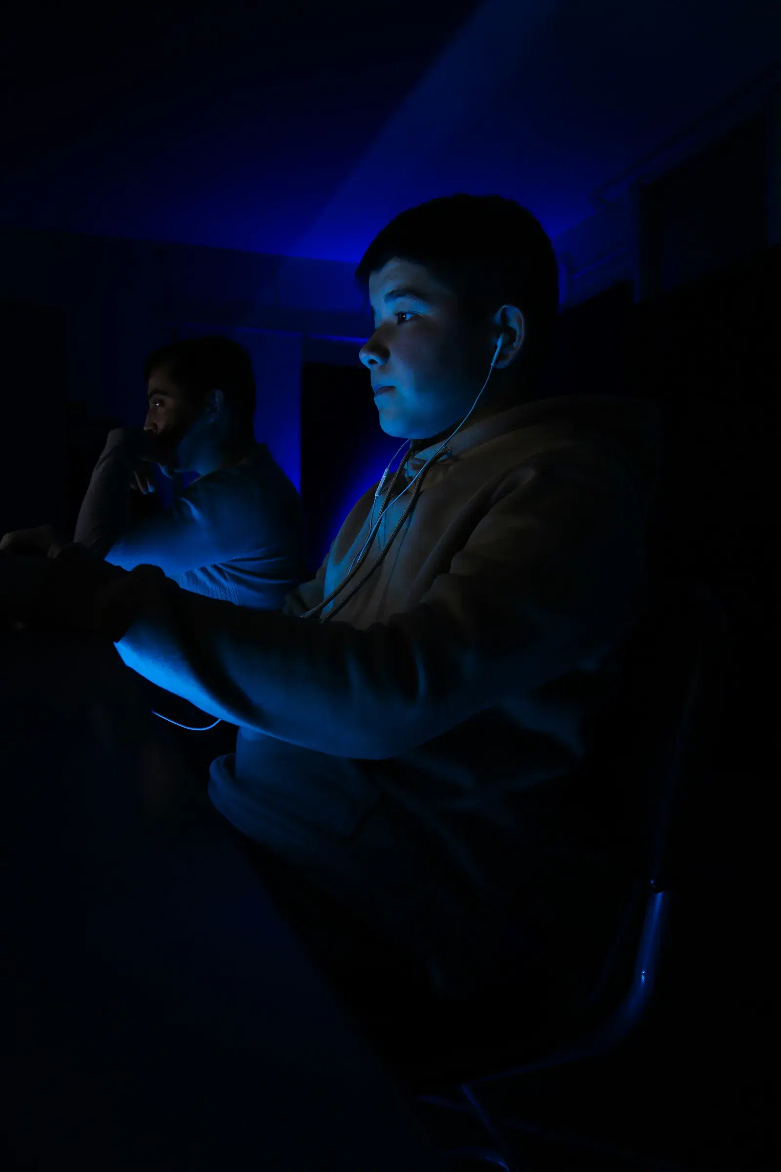 Two people at their screens in a dark room, faces lit by the displays